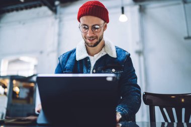 İnternette gezinmek ve tavan arasında otururken bilgi bulmak için dijital cihazda çalışan gündelik kıyafetli mutlu, yakışıklı bir erkek.