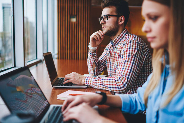 Two coworkers with open netbooks brainstorming, thoughtful man considers prospects of high technologies development while woman creates line chart using app to predict sales grows on digital market