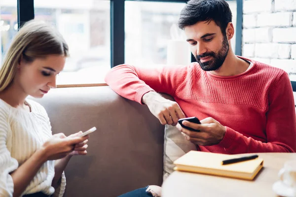 Hipster couple using smartphones gadgets prefer online chatting to real communication, Caucasian woman and man sitting in public coffee shop addicted to modern mobile phones and social networks