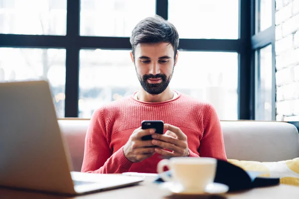 千禧年男子使用手机应用程序通过蓝牙连接使数据与上网本同步 成功的男性自由职业者使用数字技术进行在线营销和更新系统 — 图库照片