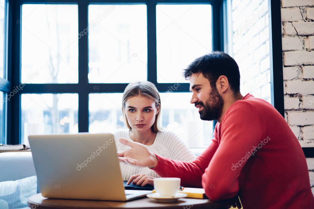Male and female freelancers cooperating indoors discussing details for common project while reading information on web page, skilled IT professionals working remotely brainstorming on program code