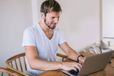 Neşeli erkek, dizüstü bilgisayardaki uygulamayla profesyonel daktilo programı kodları. Genç, pozitif hipster adam internet, iş ve serbest konsepti kullanarak bilgi arıyor.