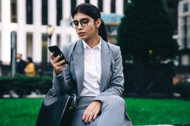 Klasik göz giyimi içinde çekici Latin girişimcinin akıllı telefon bankacılığı uygulaması üzerinden online para transferi yapması gözlüklü, cep telefonu metni yazan zeki kadın profesyonel.