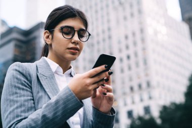 Klasik göz giyimi içinde çekici Latin girişimcinin akıllı telefon bankacılığı uygulaması üzerinden online para transferi yapması gözlüklü, cep telefonu metni yazan zeki kadın profesyonel.