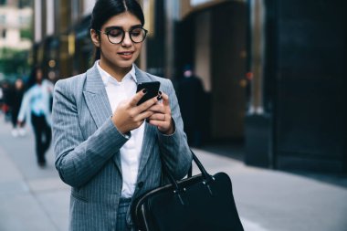 Çekici Latin kadın girişimci finansal başvuru yoluyla para alışverişini kontrol ederken şehir merkezindeki şirket toplantısına yürürken, iş kadını bankacılık için cep telefonu aygıtı kullanıyor.