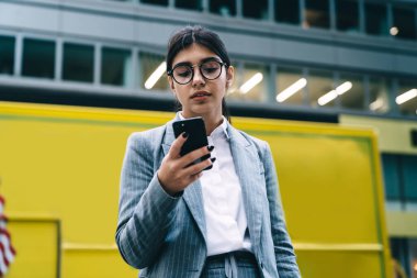 Moda gözlüklü kadın girişimci şehir merkezinde teneffüste işten haberlerle gelen mesajları okuyor, şirket çalışanı cep telefonuyla interneti taramak için 4G kablosuz kullanıyor.