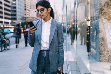 Çekici kadın analitik uzmanı cep telefonuyla finans bölgesinde caddede duran sanal müşterilerle sohbet ediyor, genç bir kadın cep telefonu cihazıyla dijital pazarlama yapıyor.