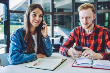 Neşeli başarılı kız öğrencinin portresi akıllı telefon aracılığıyla arkadaşlarıyla iletişim kurarken, erkek öğrenci cep telefonuyla üniversite etkinliği organizasyonunu planlamak için bilgi arıyor.