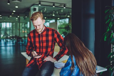 Gündelik görünümlü beyaz bir adam internet üzerinden yazı yazmak için mobil başvuru formu yazarken, kız arkadaşı yanında oturuyor ve öğreniyor, hipster adam cep telefonundan bildirimi kontrol ediyor.
