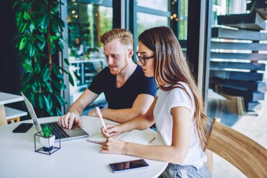 Konsantre beyaz kadın ve erkek bağımsızlar web sitesini sertifika eğitimi için izliyorlar. Dizüstü bilgisayarlı kadın üzerinde ücretsiz kablosuz bağlantı kullanıyorlar. Ana bilgileri not defterine not ediyorlar.