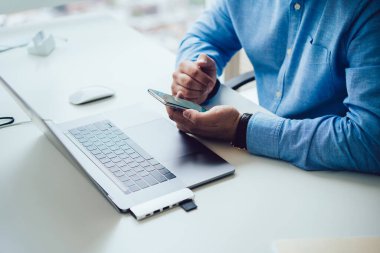 Modern ofisteki bilgisayar başında çalışan mavi gömlekli ve cep telefonu kullanan modern bir adamın ürünü.