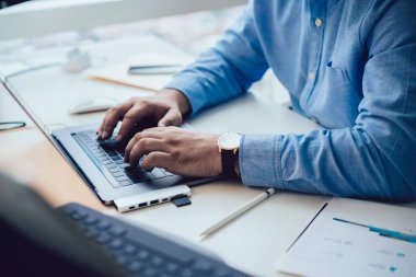 Bilgisayarda çalışan yüzü olmayan bir işadamı, modern ofisteki kağıt ve aletlerle beyaz bilgisayar masasında otururken... 