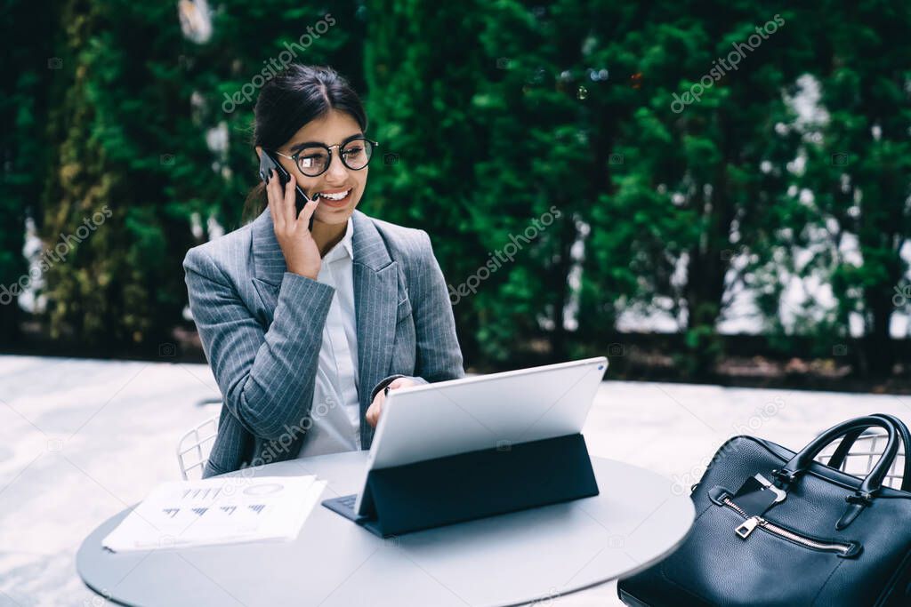 Happy cheerful Spanish female analytic expert in classic optical spectacles for provide eyes protection reading received email on touch pad and laughing calling to colleague for discussing news