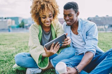 Olumlu Afro-Amerikan genç evlilik biletleri internet sitesinde, dokunmatik ped cihazında 4G internet kullanarak internetten alınıyor. Mutlu çift modern tablet sitesinde komik videolar izliyor.