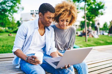 Kahveli Afrikalı Amerikalı genç bir adam dizüstü bilgisayarla internetten siyah tenli kız arkadaşıyla birlikte modern netbook 'ta yazılımları güncelliyor.
