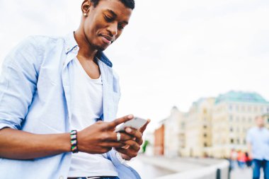 Modern şehirde yüksek hızlı 4G internet kullanarak arkadaşlarıyla online sohbet eden Afrikalı Amerikalı hipster 'ın bakış açısının altında. Cep telefonunun profilini güncelleyen koyu tenli genç adam.