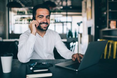 Akıllı telefondan hoşlanan başarılı bir adamın portresi iş için dizüstü bilgisayarla masada oturan, neşeli erkek CEO 'nun mobil uygulama üzerinden 4G internet kullanarak araması.