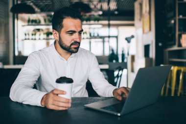 Çevrimiçi dijital pazarlama için internet üzerinden iş programlaması yapan yetenekli erkek yazılım geliştirici, iş yerinde kahve molası sırasında dizüstü bilgisayardan haber okuyan ciddi adam.