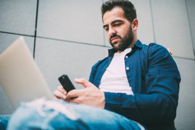 Bin yıllık hippi adamın modern dizüstü bilgisayarla şehir ortamında yeni bir başlangıç projesi olan yetenekli insan kavramını geliştirmek için otururken çevrimiçi cihaz tebligatını kontrol etmesinin altında.