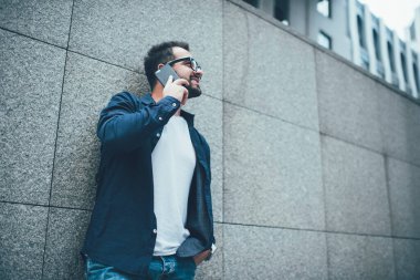 Uygulama üzerinden arama yapmak için 4G gezen internet kullanan pozitif başarılı erkek neslin yan görüntüsü, şehir ortamında iletişim kuran günlük şık giyinmiş mutlu beyaz adam