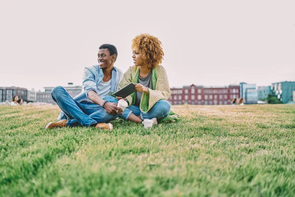 積極的なアフリカ系アメリカ人ヒップスター男笑いながら過ごすレジャー時間一緒に懐疑的なガールフレンドとともに巻き毛で公園 — ストック写真