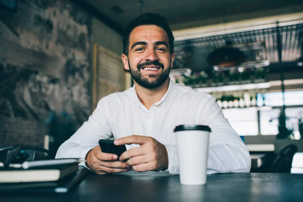 Portrait of happy successful entrepreneur with personal planner in hands smiling at camera during working day in coffee shop, positive man in casual formal wear enjoying time for creating startup idea
