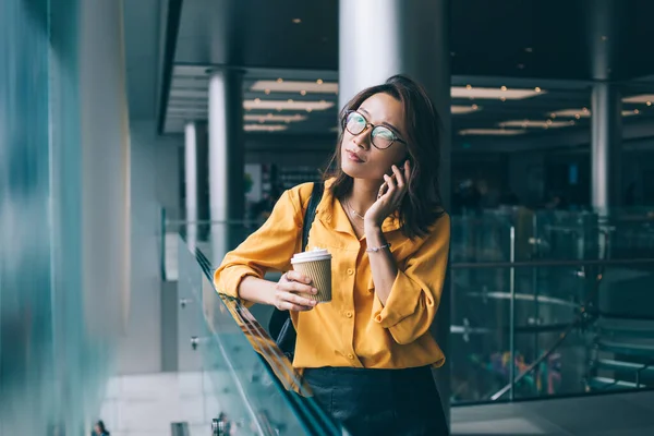 美しい焦点を当てたスリムアジアの女性グラスに紙容器コーヒーカップ思慮深く離れて見て香港のモールで電話で話して — ストック写真