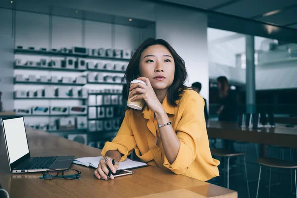 コーヒーブレイクに黄色のシャツを着たアジアの若者は 香港市内の電子機器店でラップトップでテーブルを見て離れて考えています — ストック写真