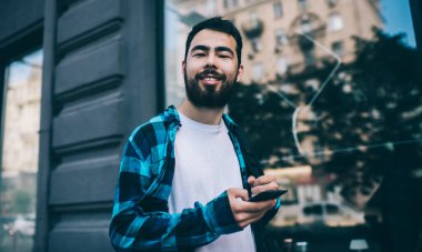 Neşeli Asyalı sakallı hippi adam kameraya bakıyor. Akıllı telefonuyla caddede duruyor. Mutlu milenyum gençleri cep telefonuyla sohbet etmek için 4G internet bağlantısı kullanıyor.