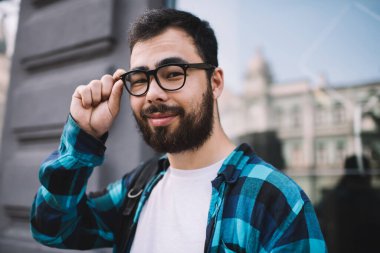 Yakışıklı, sakallı Asyalı bir adamın yarı boy portresi. Sokakta duran kameraya bakıyor. Gündelik kıyafetli genç bir erkek.