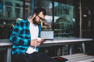 Genç Asyalı blogcu akıllı telefondan posta kontrol ediyor dışarıda çalışıyor 4G ve teknolojiyi kullanarak kullan-at kahve fincanı tutuyor, sakallı hippi adam multimedya hücresiyle paylaşıyor.