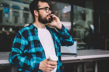 Gözlüklü genç sakallı hippi, cep telefonuyla serbest meslek hakkında konuşuyor. Uzaktan kumandayla çalışıyor. Asyalı genç adam cep telefonuyla arama yapıyor.