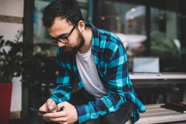 Asyalı erkek milenyum hipster göz giysisi içinde e-posta okuyor ve cep telefonundan mesajlar yolluyor, sakallı genç adam serbest ticaret yapıyor akıllı telefondaki bankacılık uygulaması ile içerik üzerine yoğunlaşıyor. 