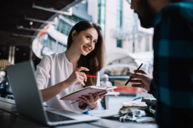 Gülümseyen beyaz kız öğrenci, arkadaşlarıyla birlikte ödev hazırlarken teknolojileri kullanıyor, iş arkadaşları, kafeteryadaki plan ve fikirleri tartışan araştırmalar yapmada işbirliği yapıyor.
