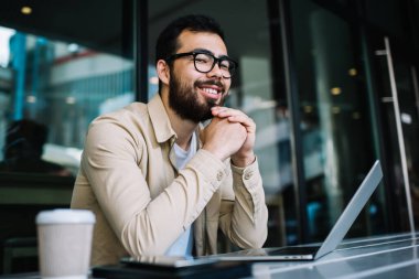 Neşeli Asyalı, vizyon koruması için gözlüklü, online iş dünyasından memnun kameraya bakan, kafedeki dizüstü bilgisayarı kullanarak eğitimden zevk alan genç, hippi bir öğrenci.