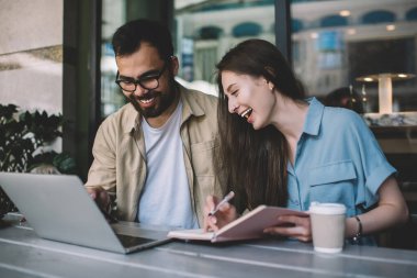 Neşeli çok ırklı çift internetten video izlerken eğleniyor. Kablosuz bağlantı ve kafeteryadaki aletleri kullanıyor. Mutlu hipster arkadaşlar boş zamanlarında dizüstü bilgisayardaki fotoğraflara bakıyor.