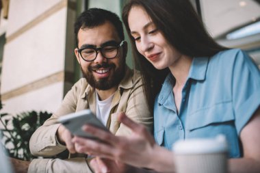 Gözlüklü neşeli Asyalı hippi kız arkadaşlarıyla cep telefonunun komik fotoğraflarına gülüyor. Kafede birlikte vakit geçiriyorlar. Akıllı telefondaki yeni güncellemelerden memnun olan erkek ve kadın arkadaşlar.