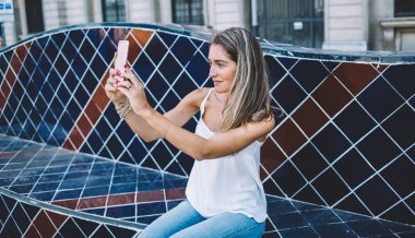 Beyaz tenli turist yaz tatillerinin tadını çıkarıyor seramik bankta oturuyor ve şehrin manzarasını fotoğraflıyor. Gündelik giyinmiş güzel bir kadın ezberlemek için fotoğraf çekiyor.