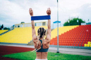 Stadyumda mavi kauçuk kurdeleyle antrenman yaparken ayakta duran ve ayağa kalkan kimliği belirsiz bir kadının arka plan görüntüsü.