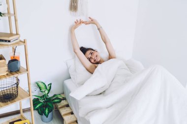 Koyu renk saçlı genç bir kadın beyaz çarşaflar ve kollarıyla yatakta yatıyor. Uyandıktan sonra geniş bir gülümsemeyle yeni bir güne başlıyor.