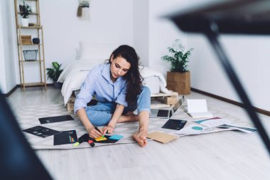 Bacak bacak üstüne atmış bir kadın, gazete ve dizüstü bilgisayarın arasında oturuyor ve sarı çıkartmaya bir şeyler yazma konusunda tutkulu. 