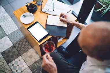 Yukarıdaki işadamının not defterine kalem yazması ve kafede çay içerken boş ekranlı tablet kullanması. 