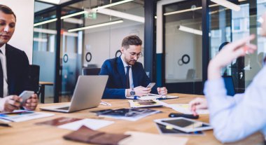 İş kıyafetleri içinde açık ofiste çalışan bir grup insan cep telefonu dokümanları ve dizüstü bilgisayarlarla internette gezinip başka yöne bakıyor. 