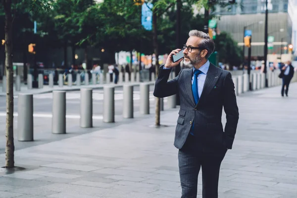 Middle aged man in suit and tie talking on phone while walking in street of New York City and looking away