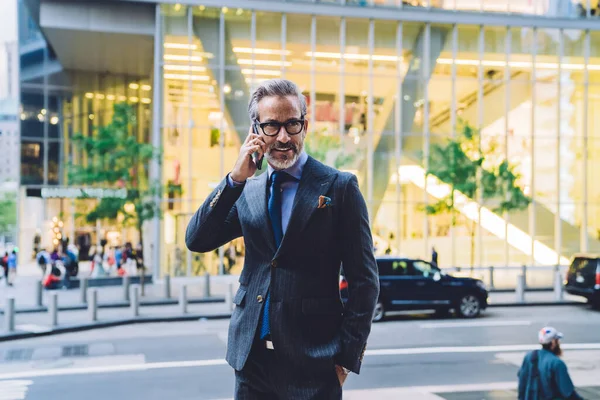 Stylish mature male in dark business suit calling on phone with enigmatic look and slight smile in New York street