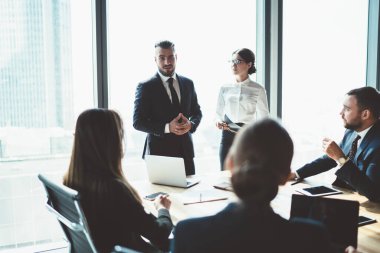 Modern konferans odasının penceresinde çeşitli aletlerle beklerken ofis çalışanlarına talimatlar veren kendinden emin bir CEO.