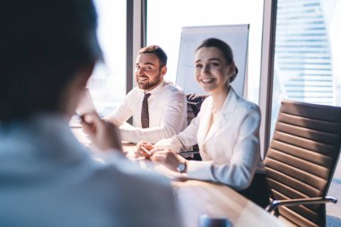 Resmi olarak gülümseyen başarılı insanların, modern şehir ofisindeki belgelerle konferans masasında otururken meslektaşlarını dinlemeleri yan görünüm. 