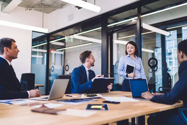 Modern toplantı odasındaki masada dizüstü bilgisayarlarla ve belgelerle çalışan çok ırklı erkek takımındaki çekici bayan.