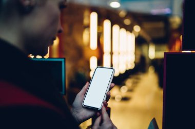 Genç bayanın pencerenin arkasındaki parlak koridorun bulanık arka planında dururken boş ekranla modern akıllı telefona göz atmasını engelle