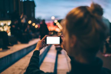 Tanımlanamayan, saçı topuz gibi olan, merdivenlerde dikilip sokak fotoğrafı çekerken boş ekrana bakan kadın yolcuların arka planı.